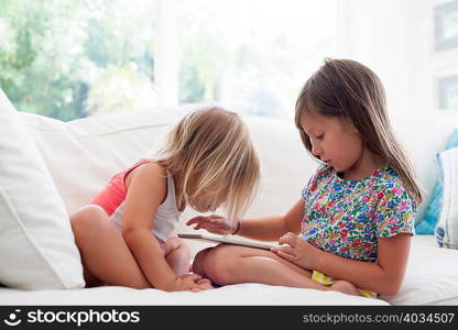 Sisters on sofa using digital tablet