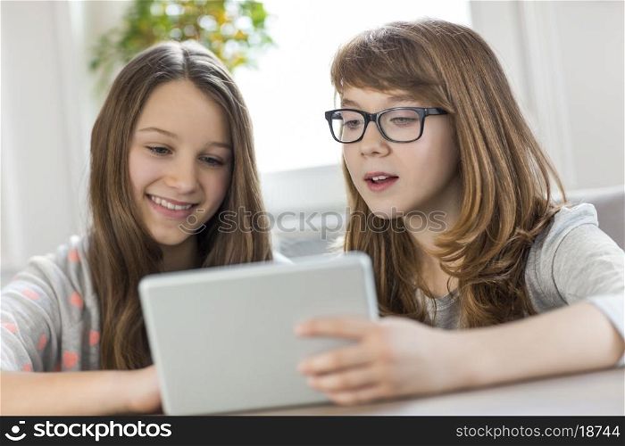 Sisters using digital tablet at table in house