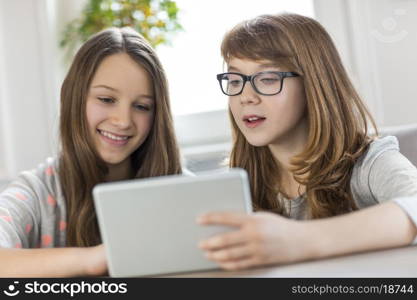 Sisters using digital tablet at table in house