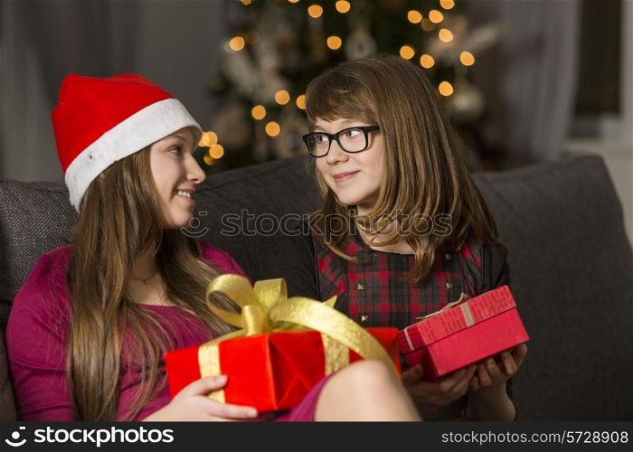 Sisters with Christmas presents looking at each other on sofa