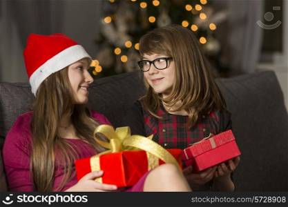 Sisters with Christmas presents looking at each other on sofa