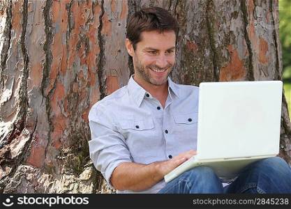 Sitting by tree with laptop
