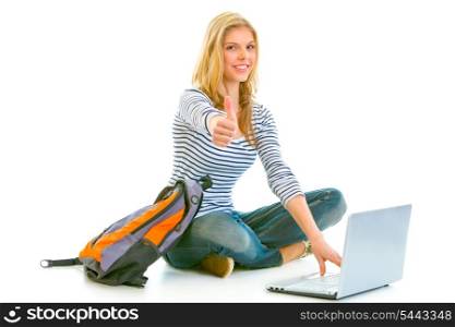 Sitting on floor with schoolbag and laptop smiling teengirl showing thumbs up gesture isolated on white &#xA;