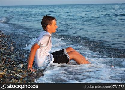 sitting teenager boy in wet clothes on stone seacoast