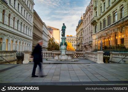 Sityscape with view of Goose Girl Fountain called Gansemadchenbrunnen in Vienna, Austria between houses and blurred walking man across the street.. Goose Girl Fountain called Gansemadchenbrunnen in Vienna, Austria.