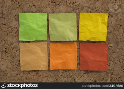 six blank crumpled sticky notes in earth colors (green, brown, yellow) on a cork bulletin board