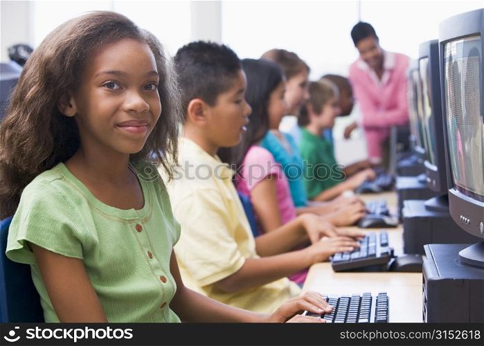 Six children at computer terminals with teacher in background (depth of field/high key)