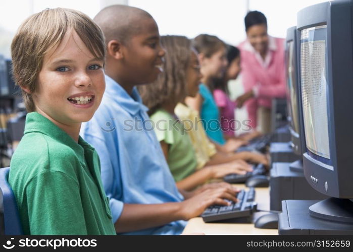 Six children at computer terminals with teacher in background (depth of field/high key)