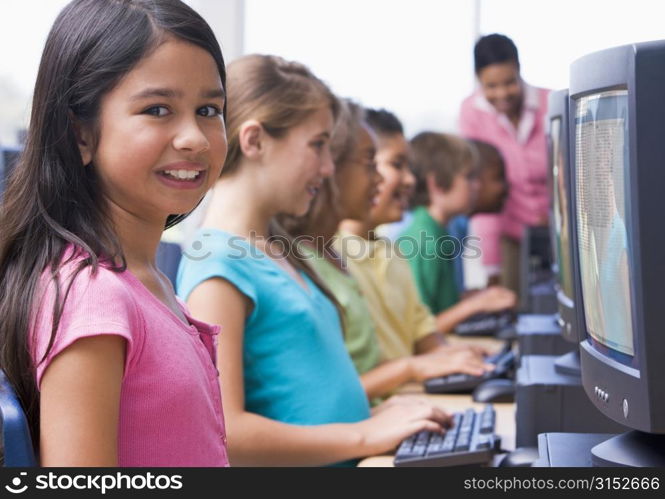 Six children at computer terminals with teacher in background (depth of field/high key)