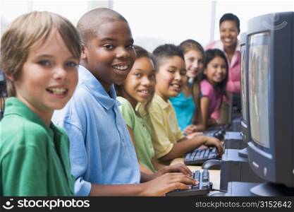 Six children at computer terminals with teacher in background (selective focus/high key)