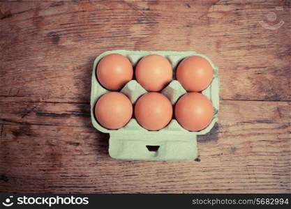 Six eggs in a cardboard tray on a wooden table