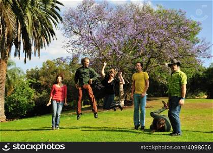 Six friends jumping and tumbling to the grass in a park in summer