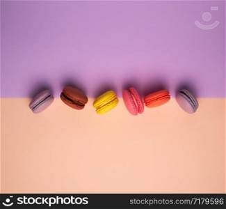 six multi-colored macarons with cream on a purple-beige background, flat lay, copy space