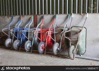 six old and rusty wheelbarrows rest against wall of farm barn