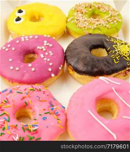 six round various sweet donuts with sprinkles in a paper white box, top view, selective focus