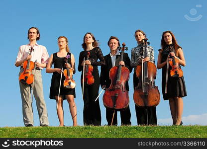 Six violinists stand on grass against sky