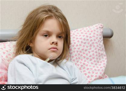 Six-year diseased girl sitting in bed and will measure the temperature of the thermometer