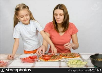 Six-year girl helps mother spread on tomato pizza