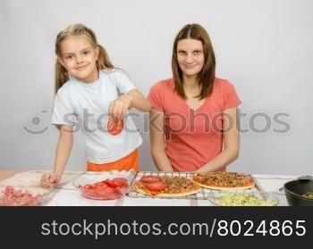 Six-year girl puts on the pizza tomatoes under the supervision of mum