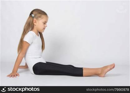 six year old girl aspiring gymnast performs a number of training exercises. Girl gymnast sitting on the floor and looks at her outstretched legs