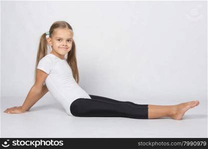 six year old girl aspiring gymnast performs a number of training exercises. Girl gymnast sitting on the floor with legs stretched and leaned back on his hands
