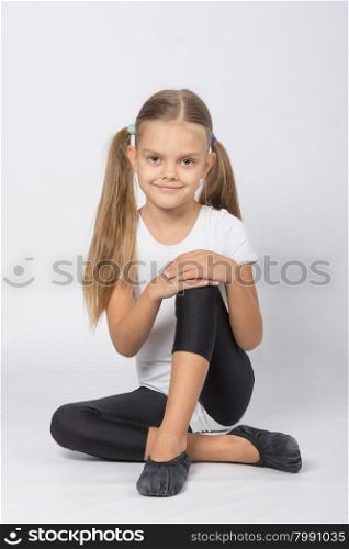 six year old girl aspiring gymnast performs a number of training exercises. Girl gymnast sitting on the floor