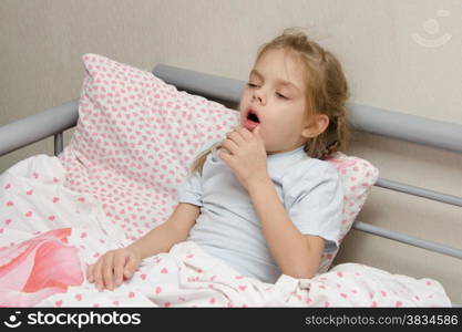 Six year old girl coughs diseased lying in bed with a thermometer on the mouse