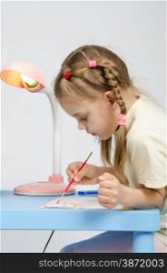 Six year old girl Europeans draws paints on a sheet of sitting at the table. Six year old girl with enthusiasm draws paints