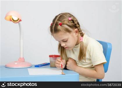 Six year old girl Europeans draws paints on a sheet of sitting at the table. Six year old girl keen on drawing