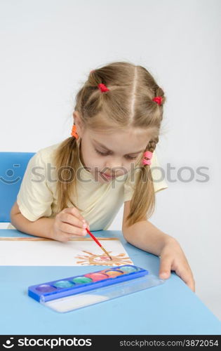 Six year old girl Europeans draws paints on a sheet of sitting at the table. Six year old girl sitting at the table and draws paints