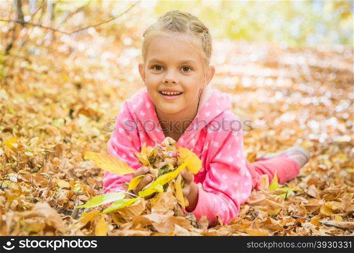 Six year old girl lying on the yellow fallen leaves
