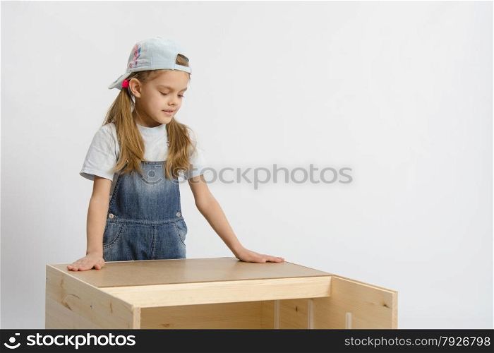 Six year old girl playing and collecting wooden cabinet. child looks at the result of assembling furniture