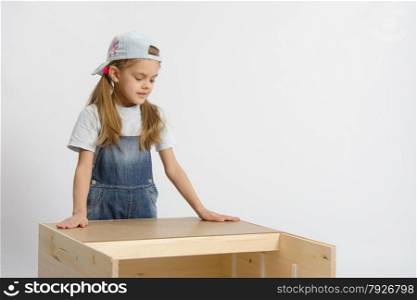Six year old girl playing and collecting wooden cabinet. child looks at the result of assembling furniture