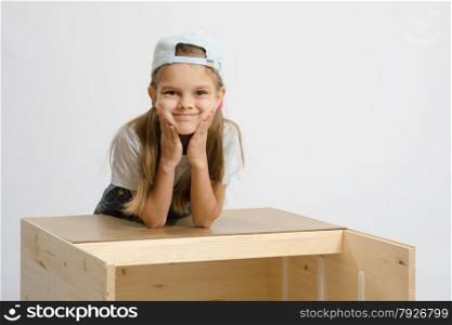 Six year old girl playing and collecting wooden cabinet. Portrait a girl leaning on back cover of chest