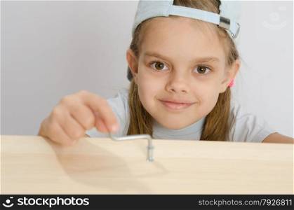 Six year old girl playing and collecting wooden cabinet. Girl twists the screw with an Allen key