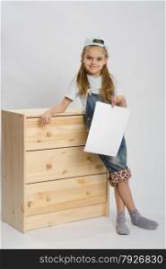 Six year old girl playing and collecting wooden cabinet. Girl in overalls collector furniture near chest with a sheet of paper