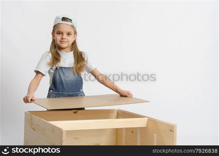 Six year old girl playing and collecting wooden cabinet. Girl collects the back cover of chest