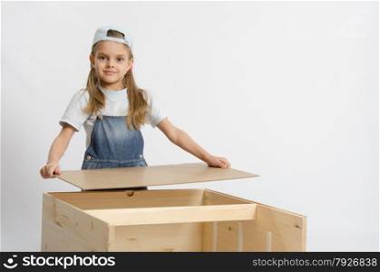 Six year old girl playing and collecting wooden cabinet. Girl collects the back cover of chest