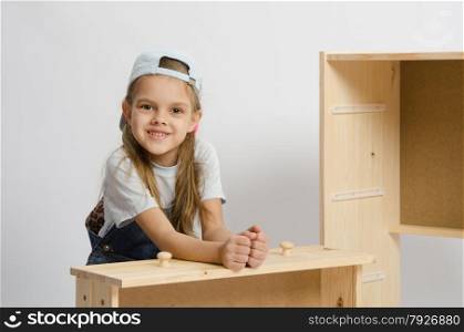 Six year old girl playing and collecting wooden cabinet. Girl sitting with an assembled frame and chest wooden box