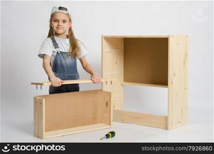 Six year old girl playing and collecting wooden cabinet. Carpenter collects drawer