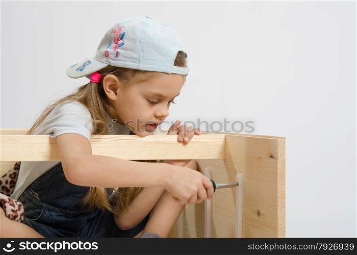 Six year old girl playing and collecting wooden cabinet. Child secures runners drawers