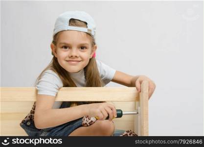 Six year old girl playing and collecting wooden cabinet. Collector of furniture screw spins