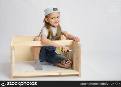 Six year old girl playing and collecting wooden cabinet. Furniture collector collects internal fastening chest
