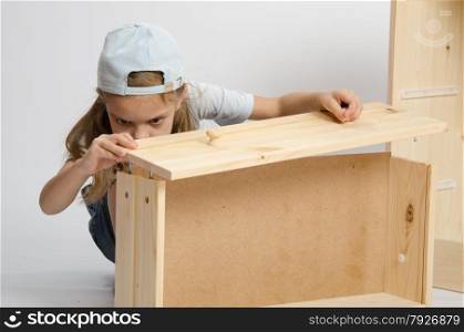 Six year old girl playing and collecting wooden cabinet. Girl collects facade box
