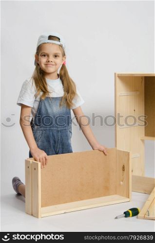 Six year old girl playing and collecting wooden cabinet. Girl collects furniture
