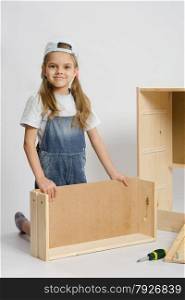 Six year old girl playing and collecting wooden cabinet. Girl collects furniture