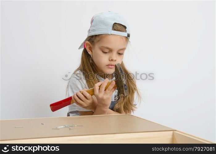 Six year old girl playing and collecting wooden cabinet. Girl holding a hammer wrong