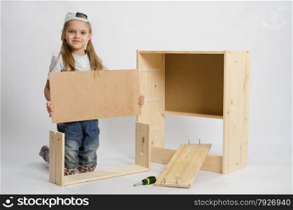 Six year old girl playing and collecting wooden cabinet. Girl sets the bottom drawer