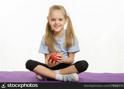 Six year old girl sitting on a rug with an apple hands. Six year old girl sitting Europeans holding an apple