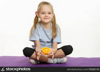 Six year old girl sitting with orange on sport mat. Six year old girl Europeans engaged in physical exercises